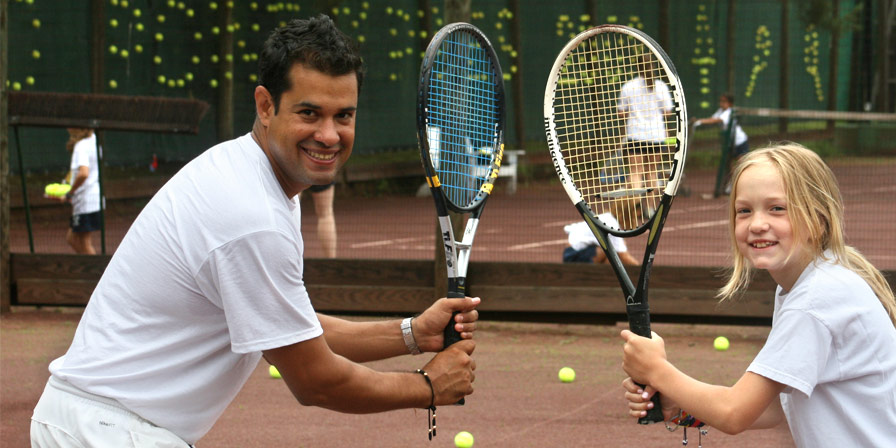 A tennis teacher and a camper hold up their rackets posing.