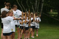 A line of campers receiving archery instruction