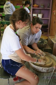 A counselor teaches a camper to spin a mug on the pottery wheel