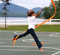 A young gymnast leaping with a ribbon in front of Brant Lake