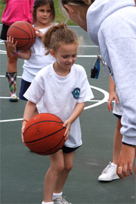 A basketball instructor teaches a young player to dribble