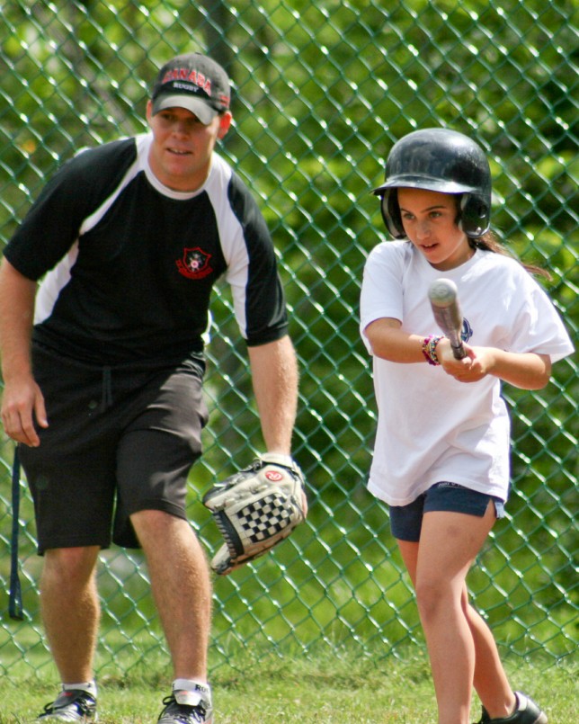 A softball instructor watches a camper's swing