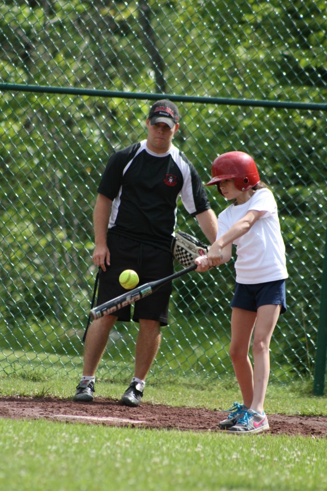 20090713024 A camper swings at a softball under the watchful eye of a coach