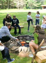 Counselors preparing breakfast over a fire for sleepy campers