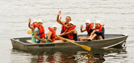 A counselor waving from a boat full of campers