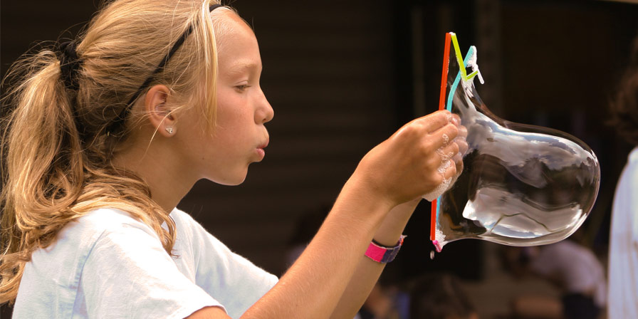A camper blowing into a big soap bubble