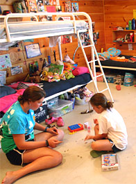 A counselor and camper playing jacks on the floor of their cabin